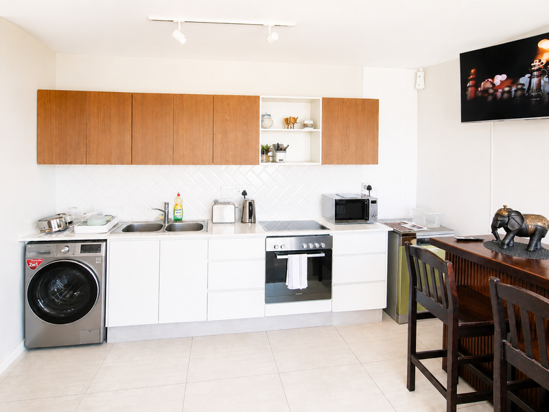 Modern kitchen featuring sleek white cabinetry, wood-tone upper cabinets, integrated oven and hob, and tiled flooring with a clean, functional layout.