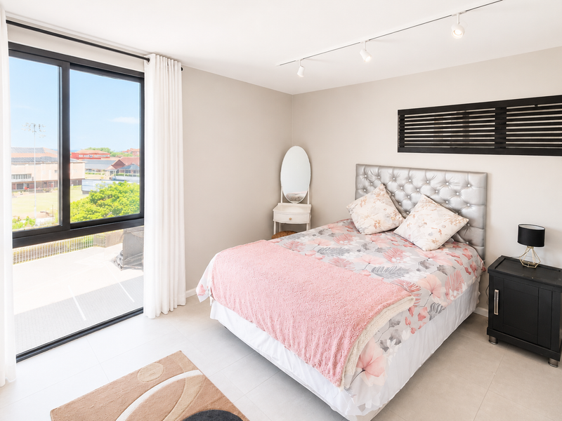 A bright and modern bedroom featuring large sliding glass doors, neutral tiled flooring, and contemporary track lighting.