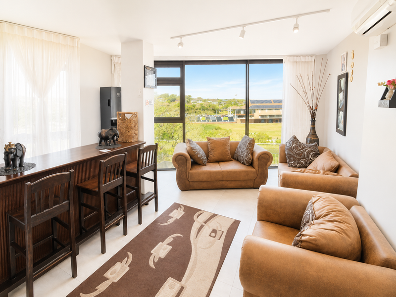 A bright, open-plan living area featuring large windows with scenic views, tiled flooring, and integrated air conditioning.