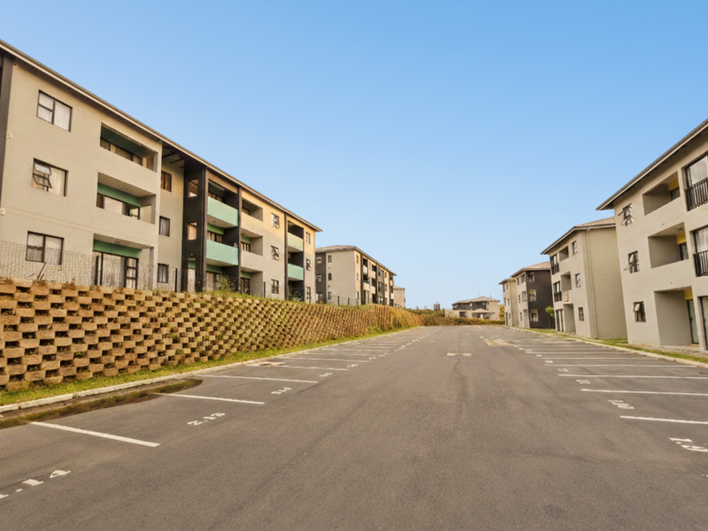 A view of the apartment complex exterior featuring paved parking bays and multi-story residential buildings with balconies.