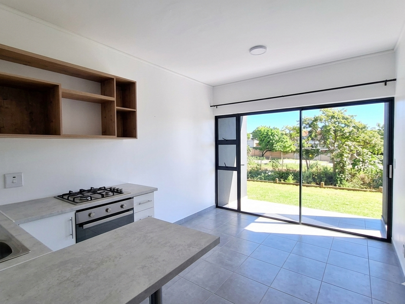Modern open-plan kitchen featuring a gas hob, built-in oven, and sleek cabinetry, flowing seamlessly through a large sliding door to a private garden area.