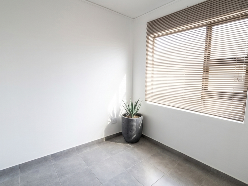 A bright, empty bedroom featuring neutral tiled flooring and fitted venetian blinds, offering a clean and versatile space ready for personalization.