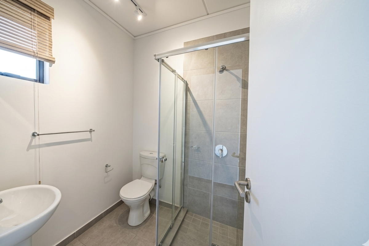 A clean, modern bathroom featuring a glass-enclosed shower, pedestal basin, and neutral floor tiling, presenting a well-maintained and functional space.