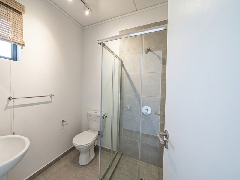 A clean, modern bathroom featuring a glass-enclosed shower, pedestal basin, and neutral floor tiling, presenting a well-maintained and functional space.