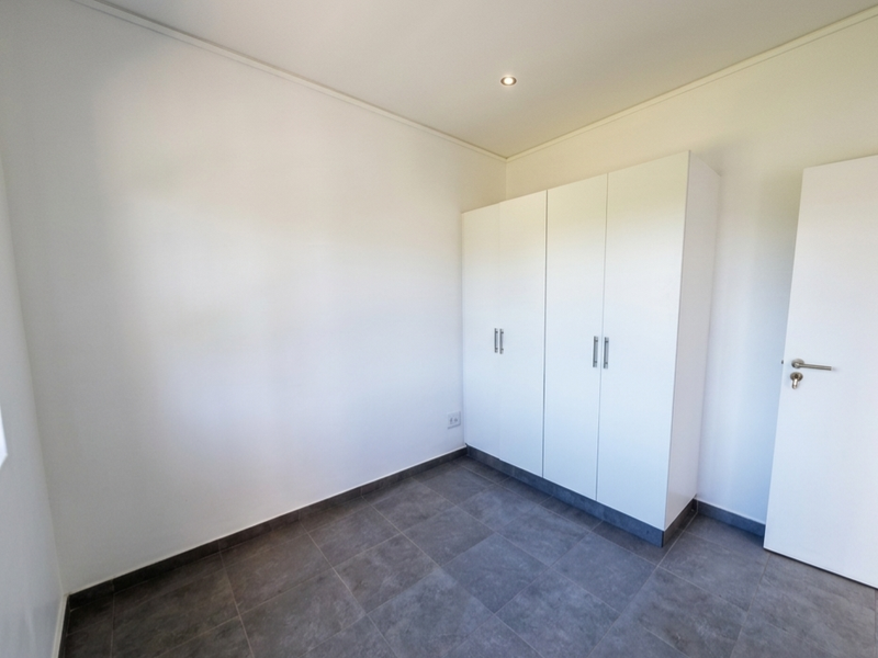 A clean, empty bedroom featuring modern grey floor tiles, a built-in white wardrobe, and neutral walls, ready for personalization.