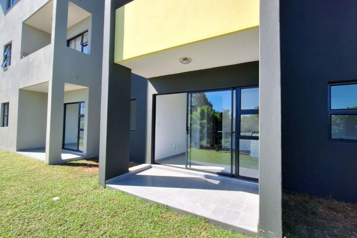 A modern apartment exterior featuring a ground-floor tiled patio with sliding glass doors and contemporary dark grey and yellow facade finishes.
