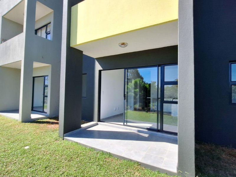 A modern apartment exterior featuring a ground-floor tiled patio with sliding glass doors and contemporary dark grey and yellow facade finishes.