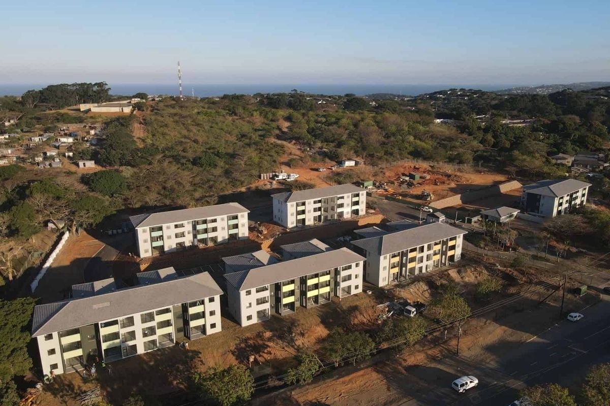 Aerial view of a modern apartment complex development featuring multiple residential blocks, paved parking, and surrounding natural landscape.