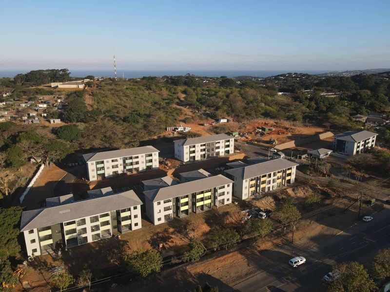 Aerial view of a modern apartment complex development featuring multiple residential blocks, paved parking, and surrounding natural landscape.