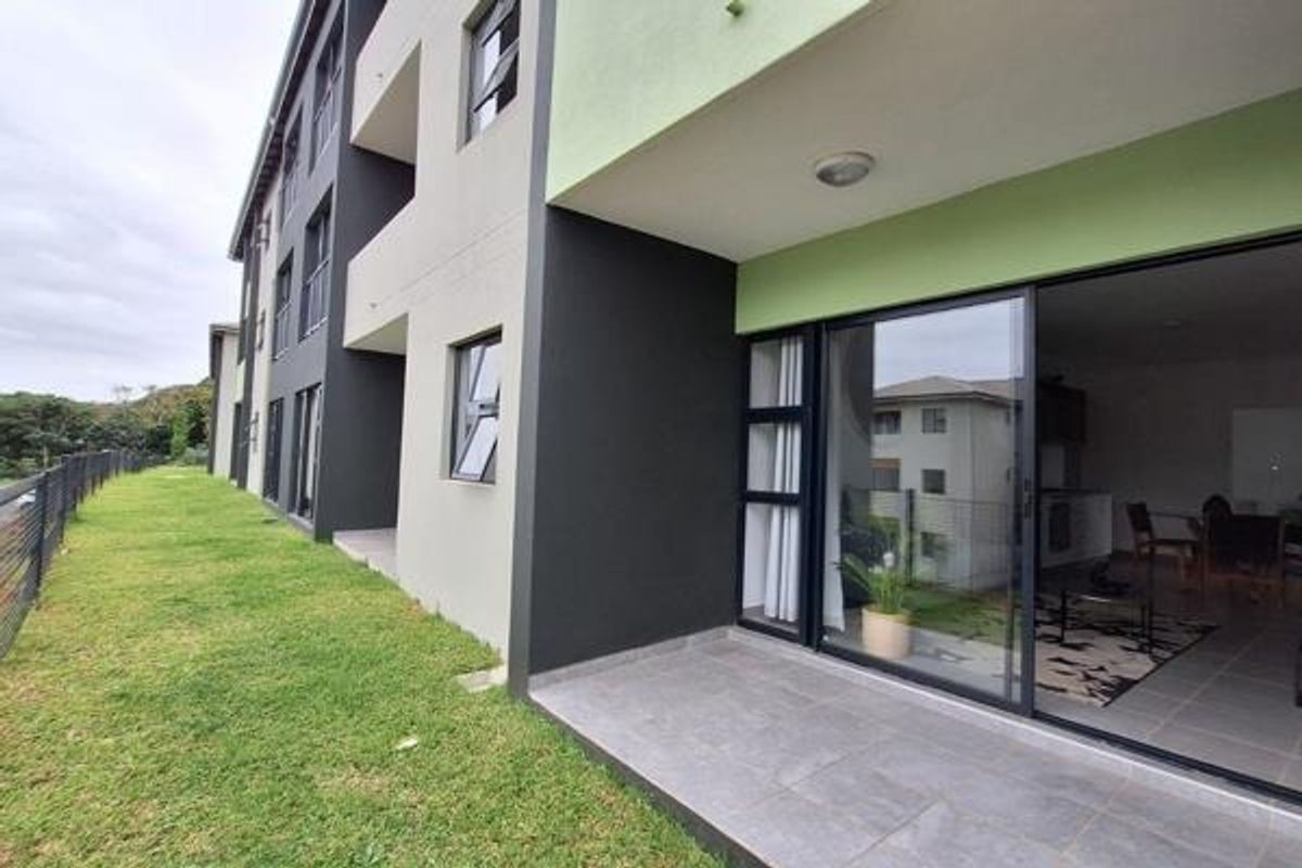 Rear view of the apartment building featuring a tiled patio area with sliding glass doors and access to the surrounding lawn.