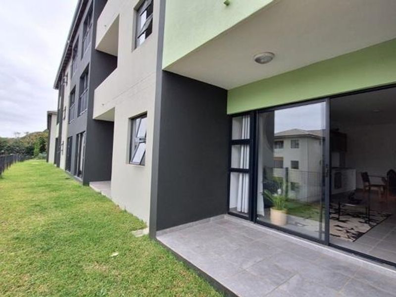 Rear view of the apartment building featuring a tiled patio area with sliding glass doors and access to the surrounding lawn.