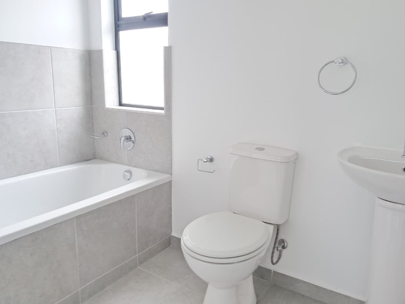 A clean, modern bathroom featuring a neutral tiled bathtub surround, pedestal basin, and standard toilet, offering a bright and functional space.
