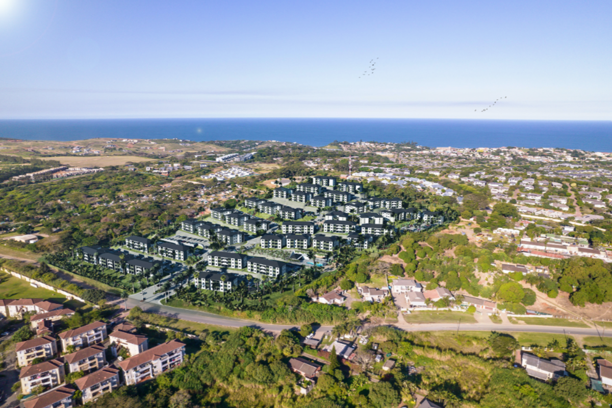 An aerial view of a modern residential apartment complex situated in a coastal area with surrounding greenery and ocean views.