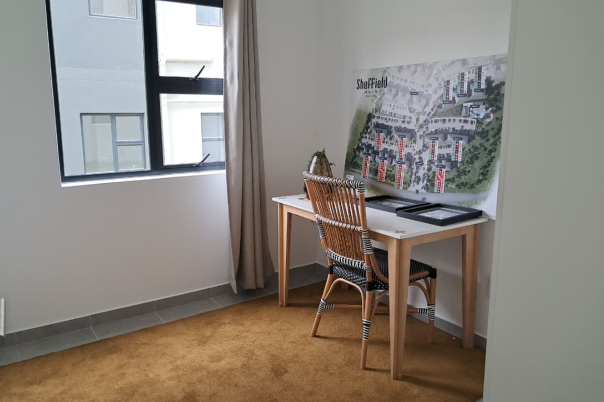 A bright bedroom featuring neutral walls, tiled flooring, and a large window with aluminium frames, offering a clean and functional space.