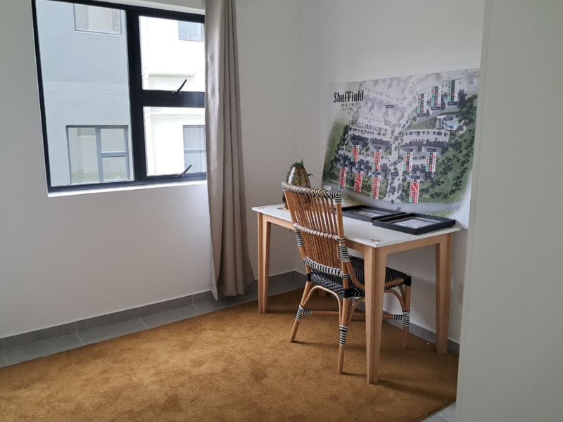 A bright bedroom featuring neutral walls, tiled flooring, and a large window with aluminium frames, offering a clean and functional space.