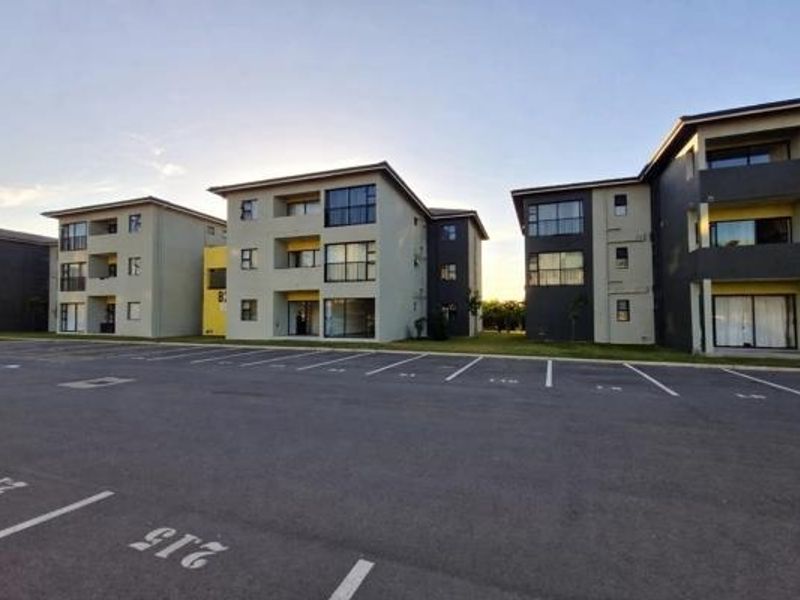 Exterior view of multi-story apartment buildings featuring paved parking area and private balconies.
