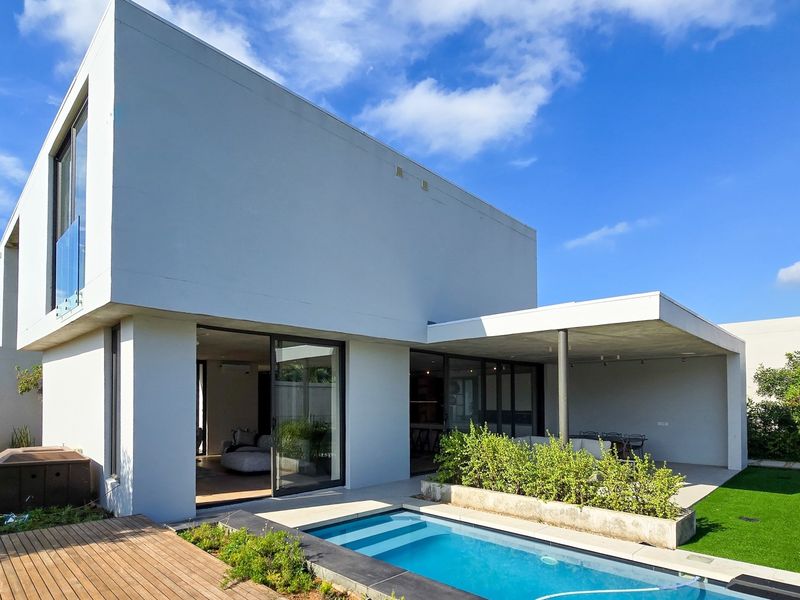Modern rear exterior featuring a swimming pool, covered patio area, timber decking, and clean architectural lines with large sliding glass doors.