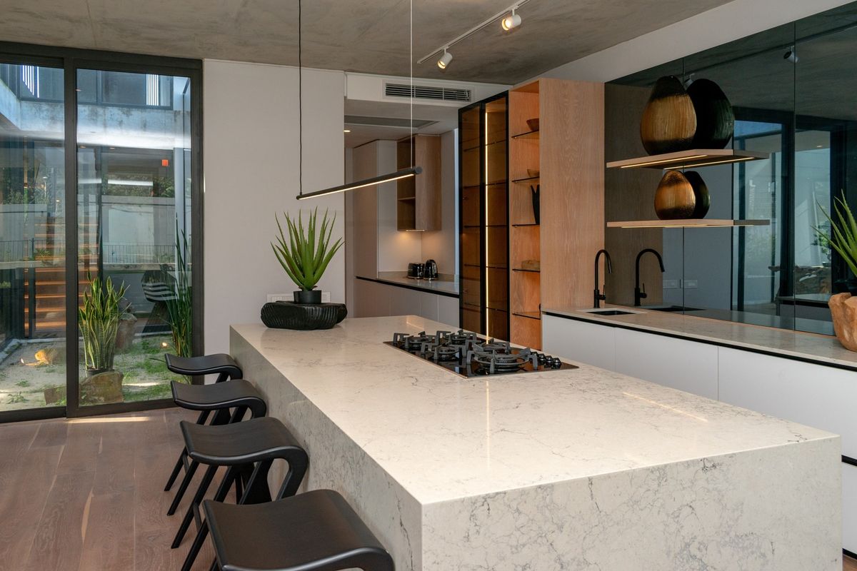 Modern kitchen featuring a large stone island with integrated gas cooktop, sleek cabinetry, mirrored splashback, and direct access to an outdoor courtyard.