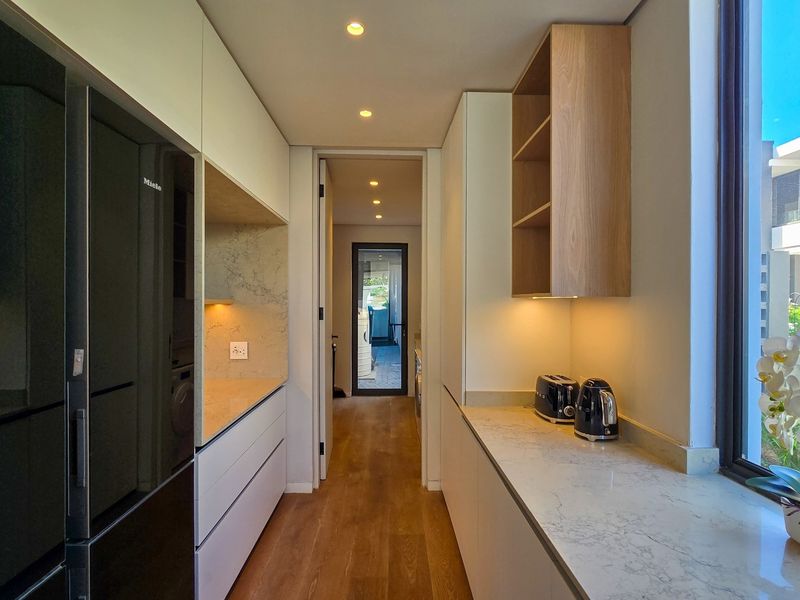 Modern scullery featuring sleek built-in cabinetry, stone countertops, integrated appliances, and warm recessed lighting, providing a functional and stylish secondary kitchen space.