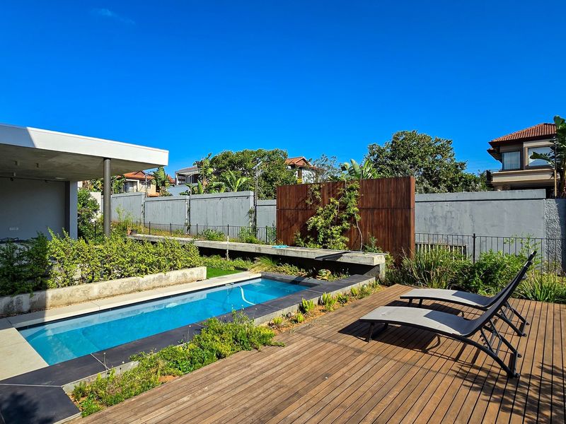 Modern outdoor entertainment area featuring a swimming pool, timber decking, concrete planters, and a covered patio space.