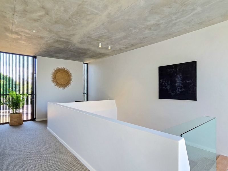 A modern, minimalist landing area featuring an exposed concrete ceiling, glass balustrade, and a striking vertical slat screen door.