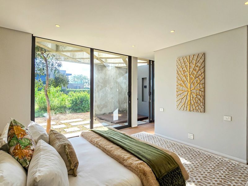 Modern bedroom featuring floor-to-ceiling sliding glass doors, recessed lighting, and built-in storage, offering seamless access to the outdoor garden area.
