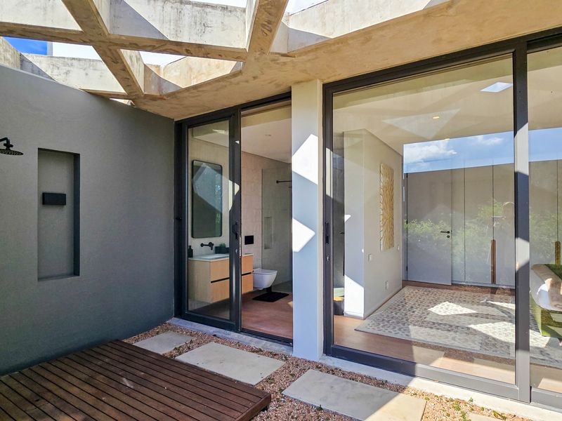 Modern outdoor patio featuring a unique concrete pergola, timber decking, and an integrated outdoor shower, seamlessly connecting to the interior living space.