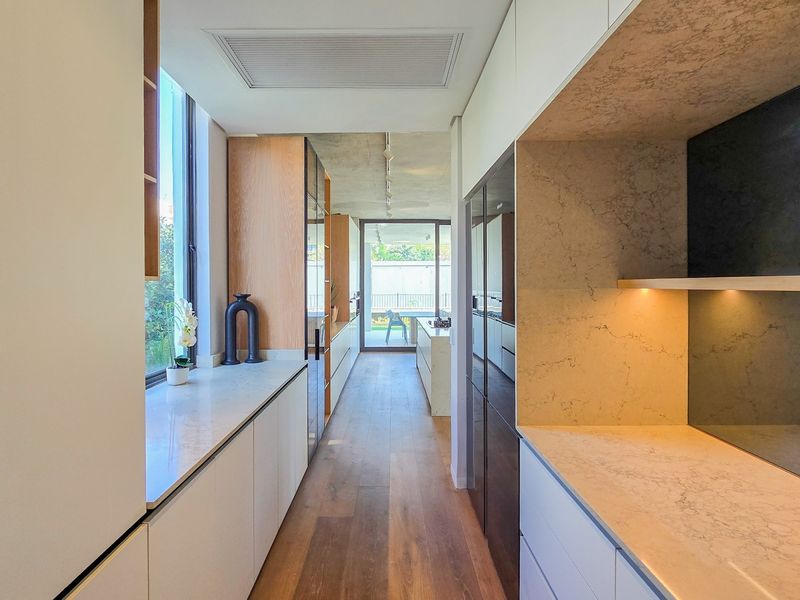 A modern, high-end scullery featuring sleek built-in cabinetry, stone countertops, and premium hardwood flooring, leading directly to an outdoor patio area.