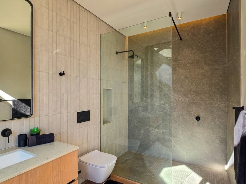 Modern bathroom featuring a walk-in shower with glass screen, wall-mounted toilet, and a sleek vanity with contemporary black matte fixtures.