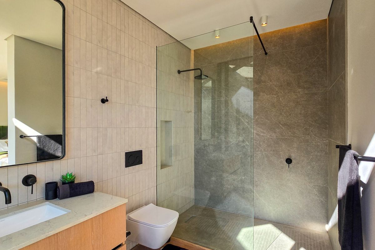 Modern bathroom featuring a walk-in shower with glass screen, wall-mounted toilet, and a sleek vanity with contemporary black matte fixtures.