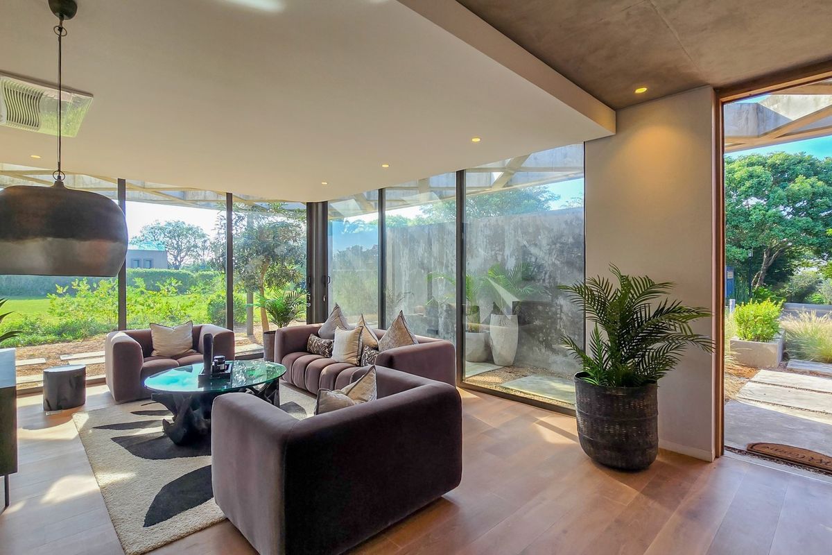 Modern living room featuring expansive floor-to-ceiling glass walls, hardwood flooring, and a seamless transition to the outdoor garden area.