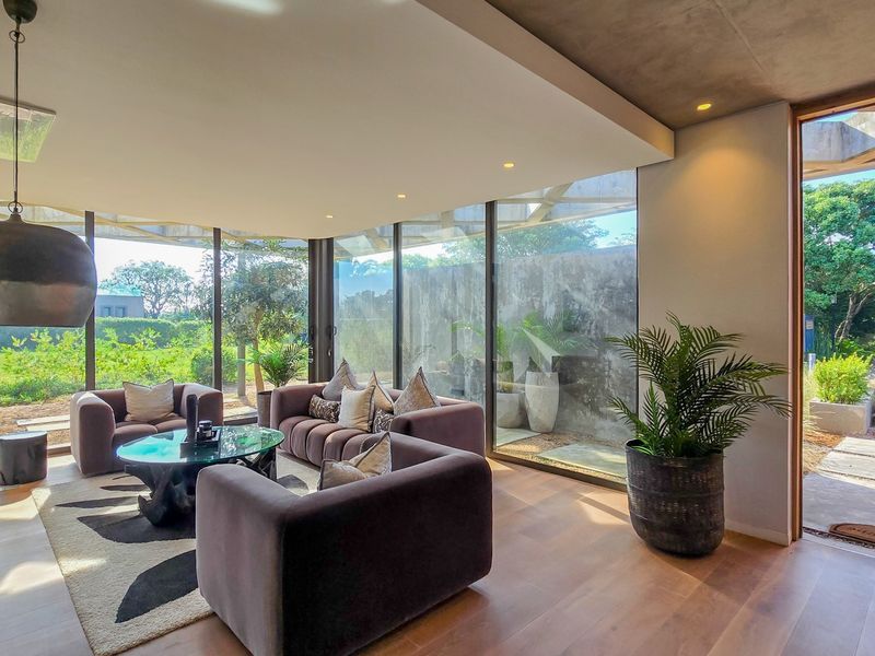Modern living room featuring expansive floor-to-ceiling glass walls, hardwood flooring, and a seamless transition to the outdoor garden area.