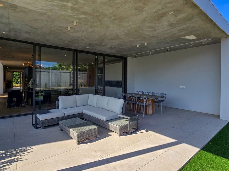 Spacious covered patio featuring a modern concrete ceiling, recessed lighting, and large format floor tiles, seamlessly connecting to the interior through sliding glass doors.