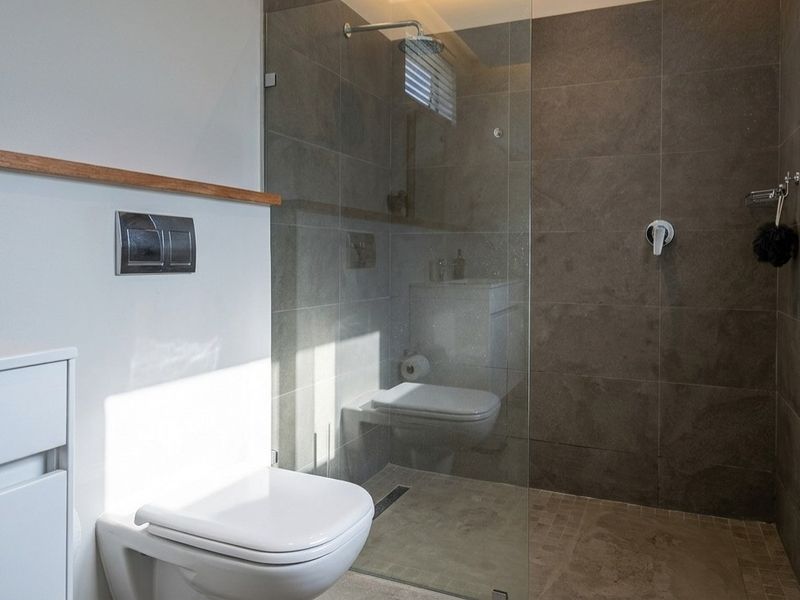 Modern bathroom featuring a wall-mounted toilet, a spacious walk-in shower with a glass screen, and contemporary grey tiling.