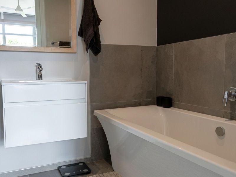 Modern bathroom featuring a wall-mounted vanity, sleek basin, and a contemporary bathtub with wall-mounted mixer tap and grey tiled splashback.