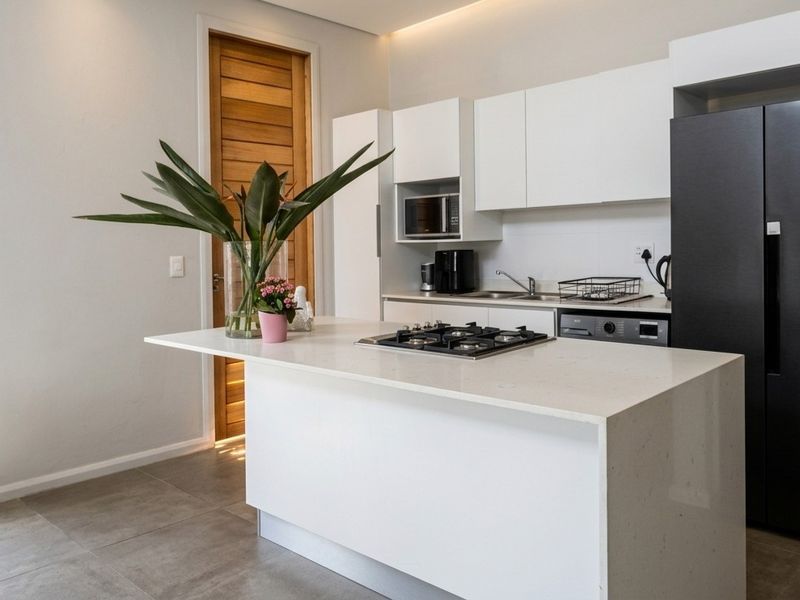 Modern kitchen featuring a central island with a gas hob, sleek white cabinetry, built-in microwave, and high-quality tiled flooring.