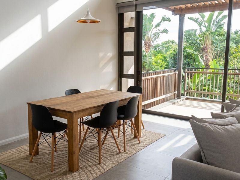 Bright open-plan living and dining area featuring large sliding doors that open onto a private balcony with lush garden views.