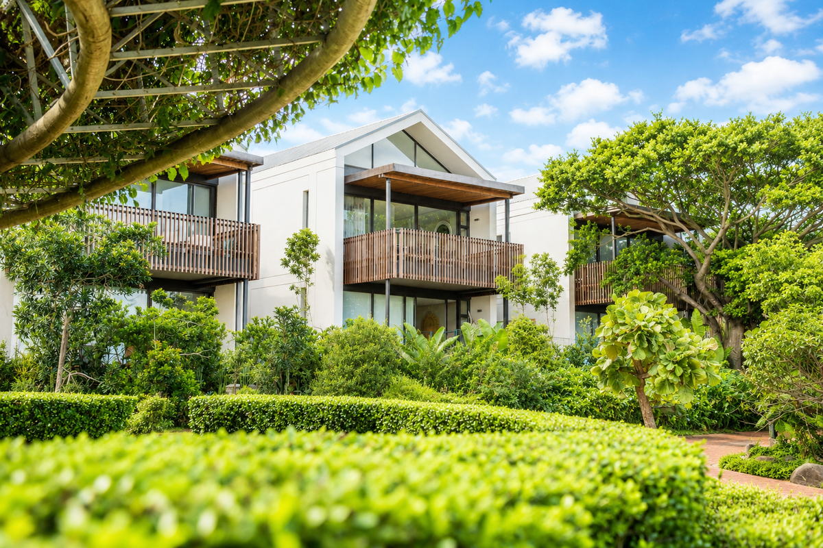 A view of modern apartment units featuring timber balcony screens, pitched roof architecture, and lush, well-maintained landscaped gardens.