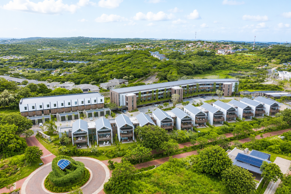 Aerial view of a modern residential apartment complex featuring multiple units, landscaped grounds, and paved access roads in a lush green setting.