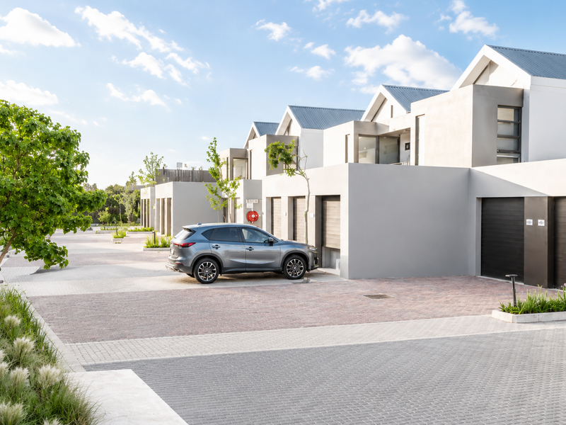A modern residential complex featuring a paved driveway, integrated garage doors, and well-maintained landscaped garden beds.