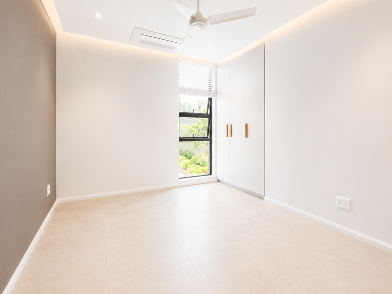 A bright, modern, and empty bedroom featuring tiled floors, built-in cupboards, a ceiling fan, and ducted air conditioning.