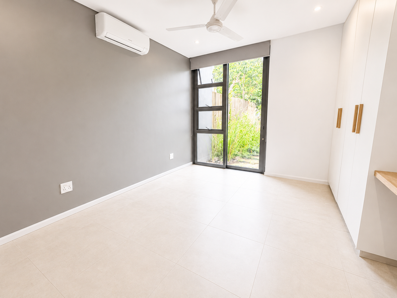 A bright, modern bedroom featuring neutral tones, tiled flooring, built-in wardrobes, a split-system air conditioner, and direct access to a private outdoor area.