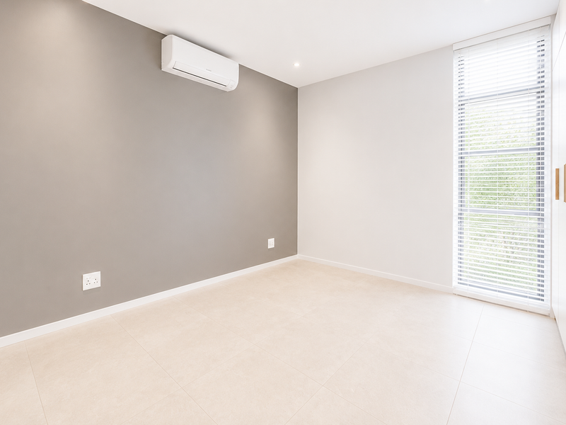 A bright, modern, and empty bedroom featuring neutral tones, tiled flooring, a split-system air conditioner, and built-in wardrobe storage.