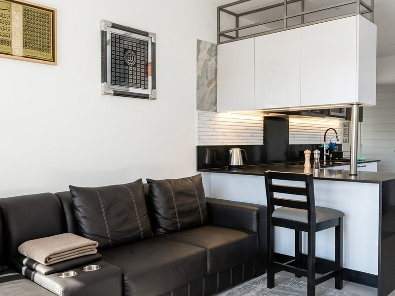 Modern open-plan living area featuring a compact kitchen with white cabinetry, black granite countertops, and a functional breakfast bar island.