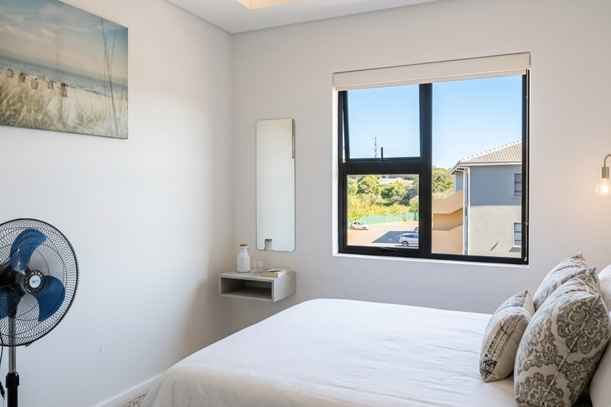 A bright, modern bedroom featuring a black aluminium window frame, roller blind, and a convenient wall-mounted floating shelf.