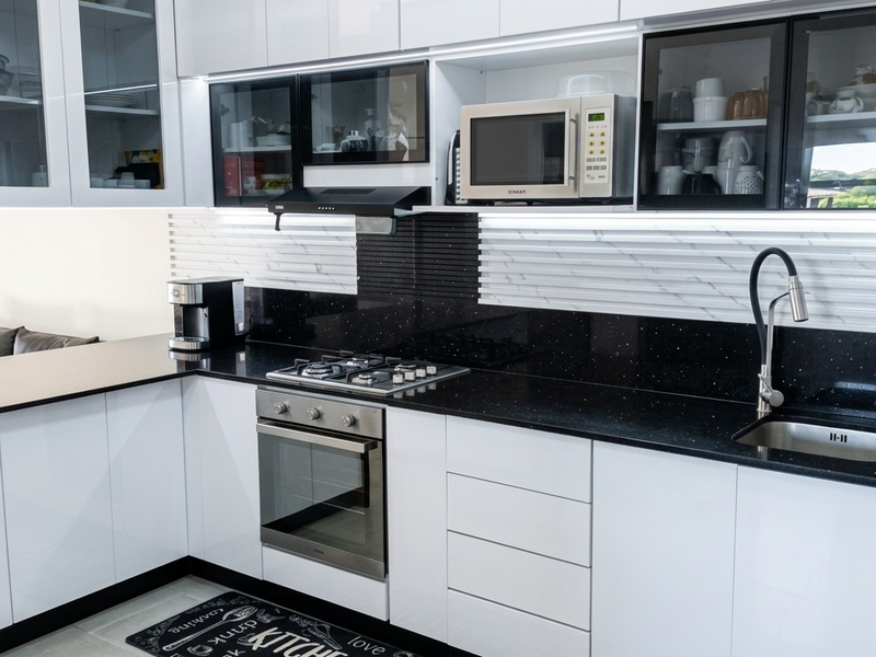 Modern kitchen featuring white cabinetry, black quartz countertops, integrated appliances, and stylish marble-effect backsplash with under-cabinet lighting.