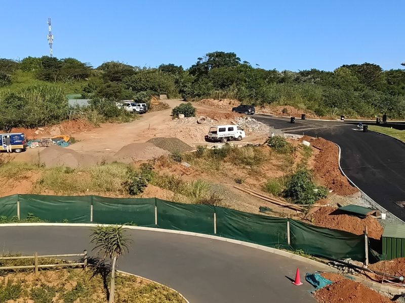 An aerial view of a residential development site showing ongoing road construction, earthworks, and proximity to an existing apartment building.