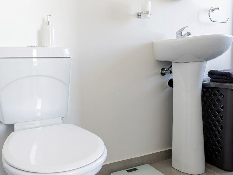 A clean and functional bathroom featuring a white pedestal basin with chrome mixer tap and a standard toilet.