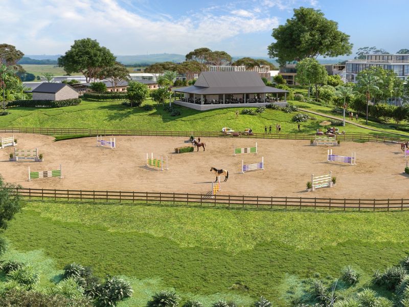 An aerial view of a professional equestrian arena featuring show jumping obstacles, post and rail fencing, and surrounding landscaped grounds.