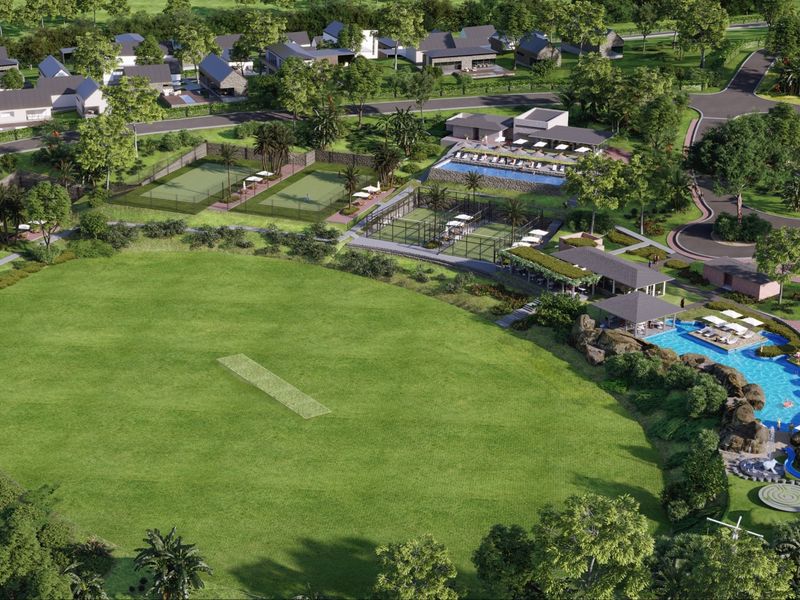 Aerial view of a residential estate featuring a cricket pitch, tennis courts, swimming pool, and clubhouse facilities within a landscaped community setting.
